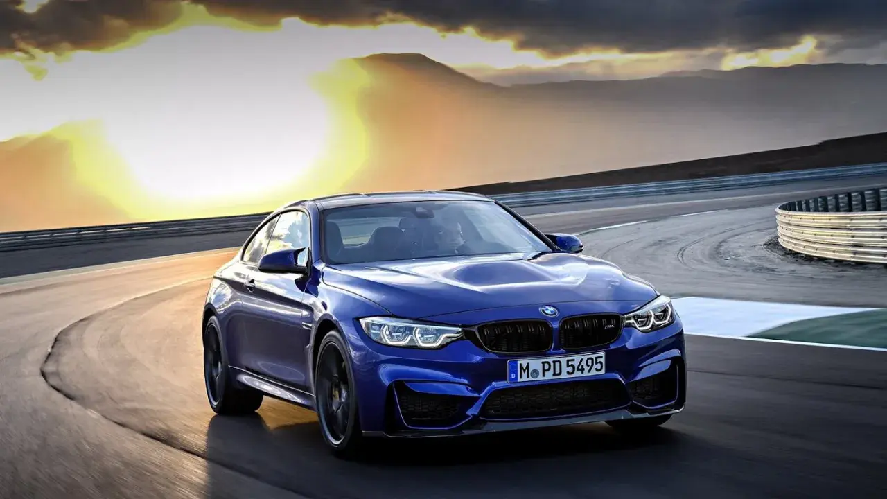 Niebieskie BMW M2 CS pędzi po torze wyścigowym podczas zachodu słońca.