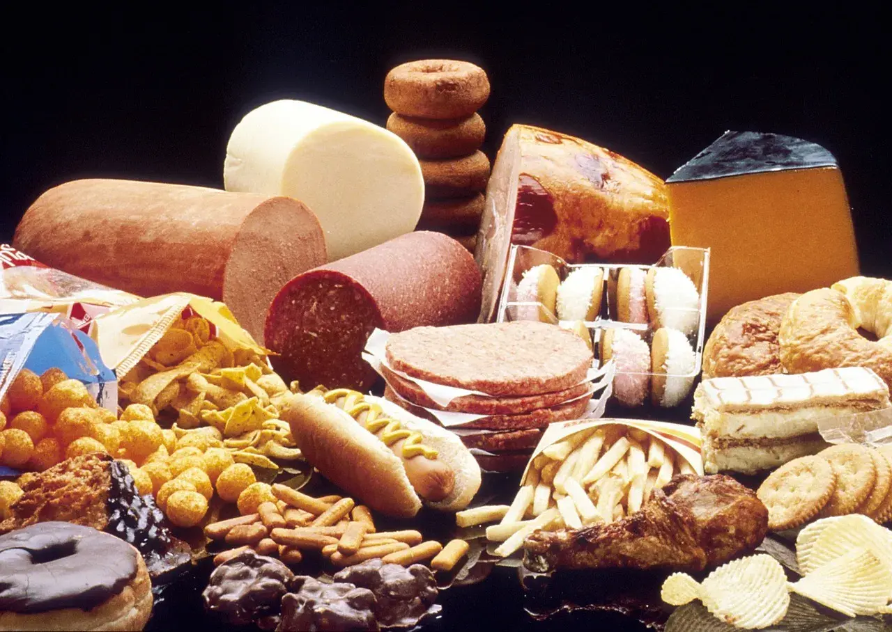 Stół ugina się pod ciężarem przetworzonej żywności: wędliny, sery, frytki, słodycze, ciastka, pączki, hamburgery i chipsy – to wszystko zawiera tłuszcze trans.