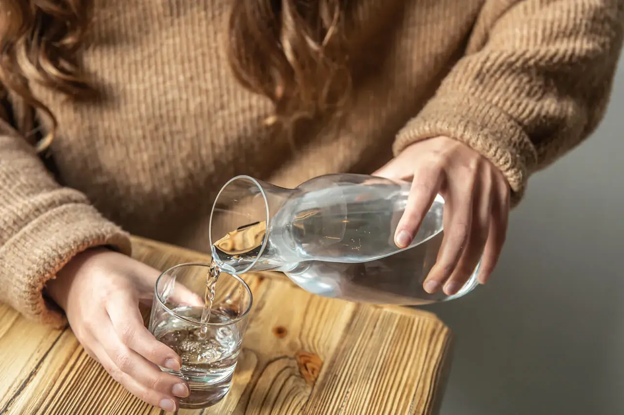Dłonie nalewają wodę z karafki do szklanki. Pamiętaj, by stay hydrated.