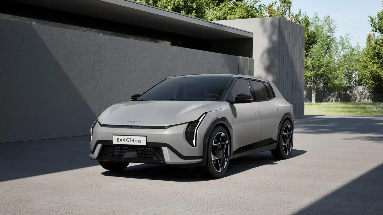Nowoczesny, jasnoszary Kia EV4 GT-Line stoi na podjeździe przed minimalistycznym budynkiem.