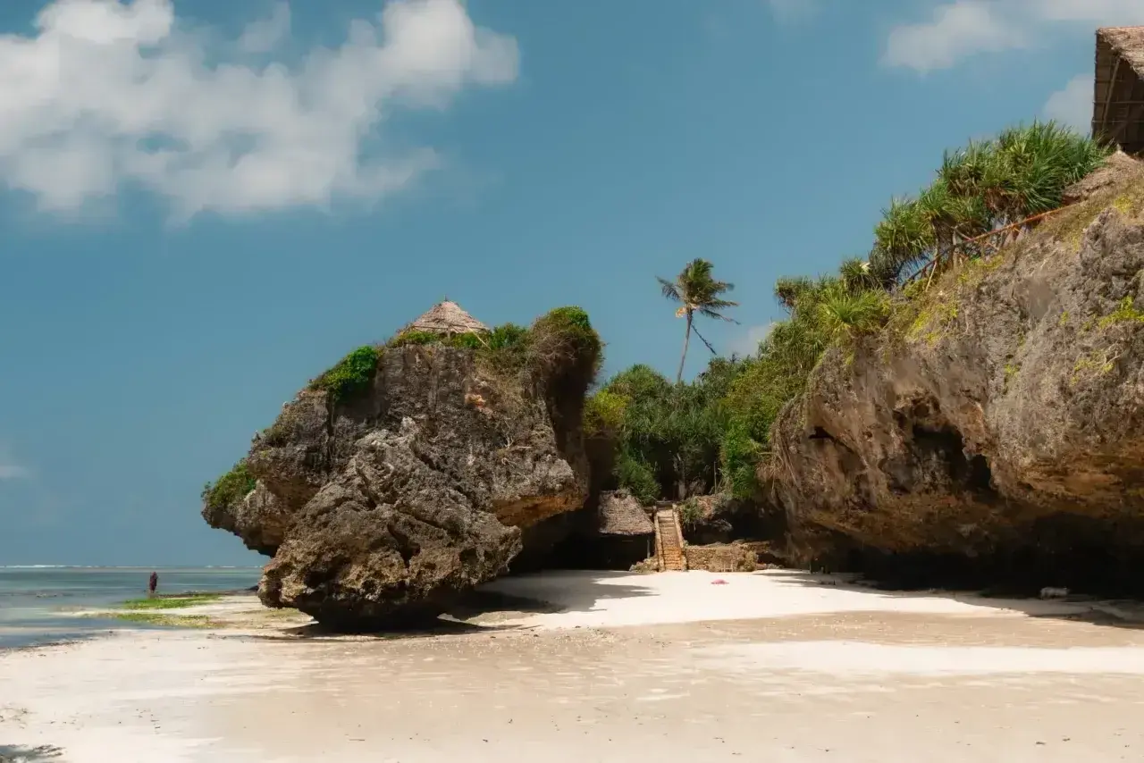 Piękna plaża na Zanzibarze w kwietniu. Skaliste klify, palmy i chatki z trawy tworzą rajski krajobraz.