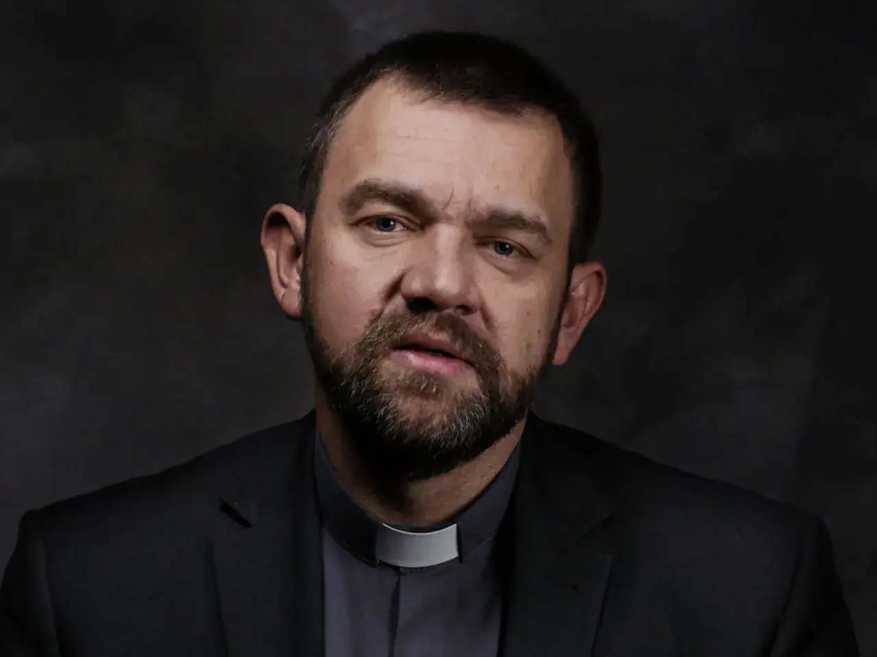 Duchowny z brodą, w czarnym garniturze i z białą kolaretką, spogląda zamyślony. Czy Bóg nas testuje?