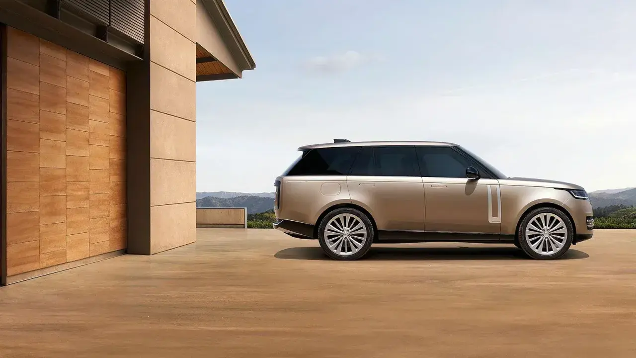 Elegancki Range Rover w kolorze piaskowym, zaparkowany przed nowoczesnym domem z drewnianymi drzwiami. Sprawdź range rover cena!