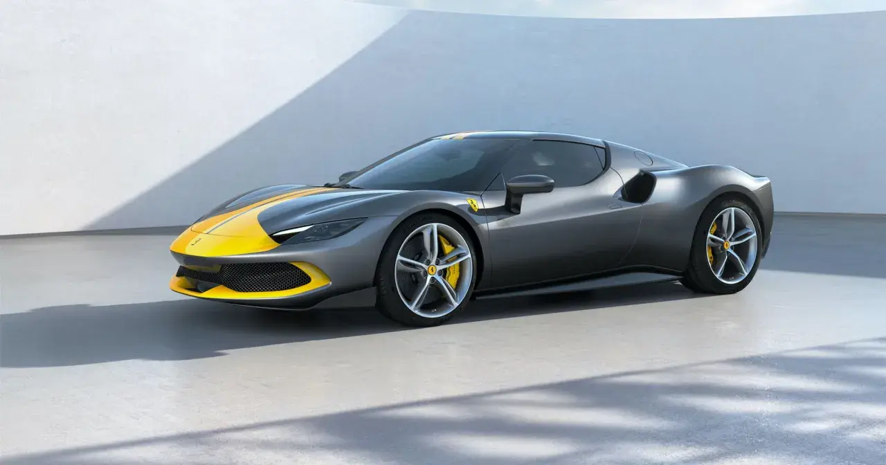 Szary Ferrari 296 GTB z żółtymi pasami na masce i dachu, stojący na betonowej posadzce.