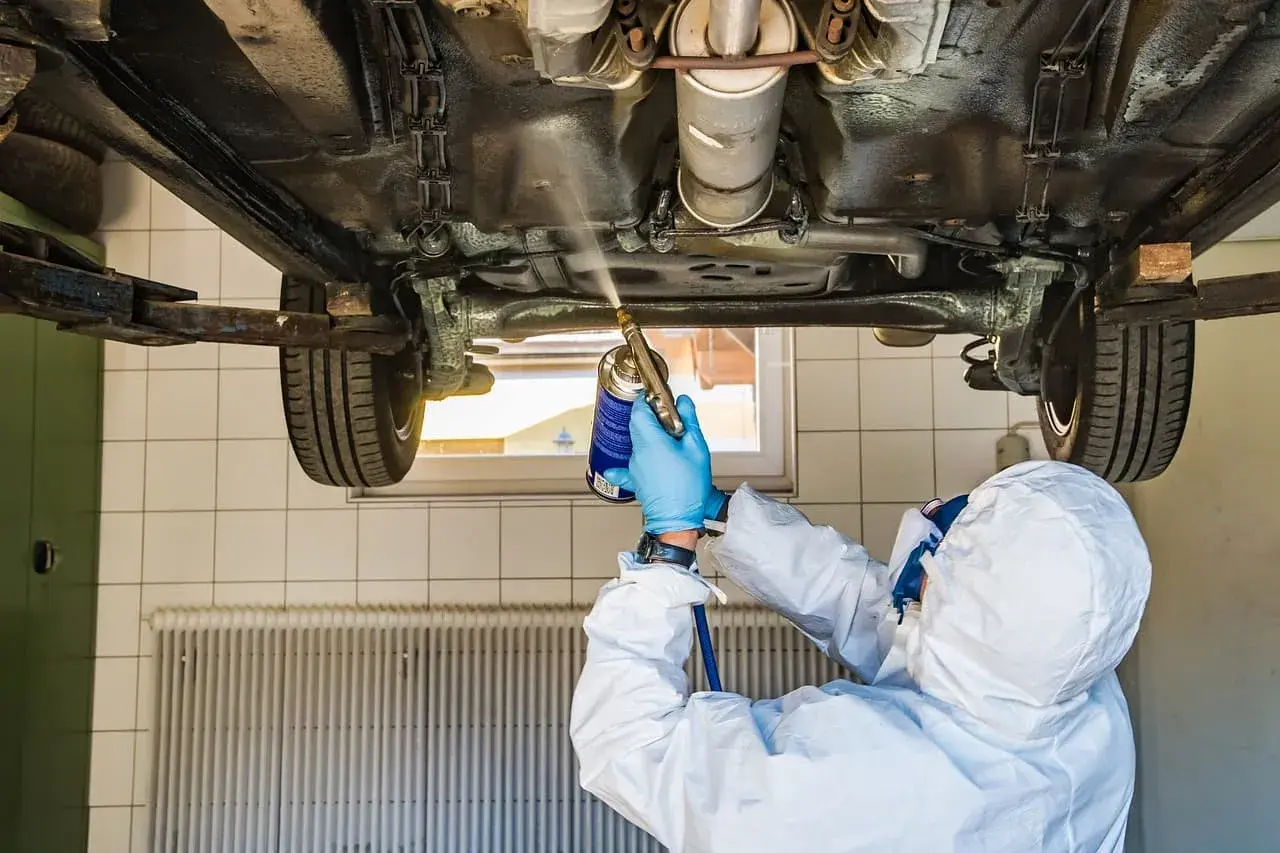 Mechanik w kombinezonie zabezpieczającym podwozie samochodu. Zastanawiasz się, ile kosztuje przegląd samochodu z gazem?