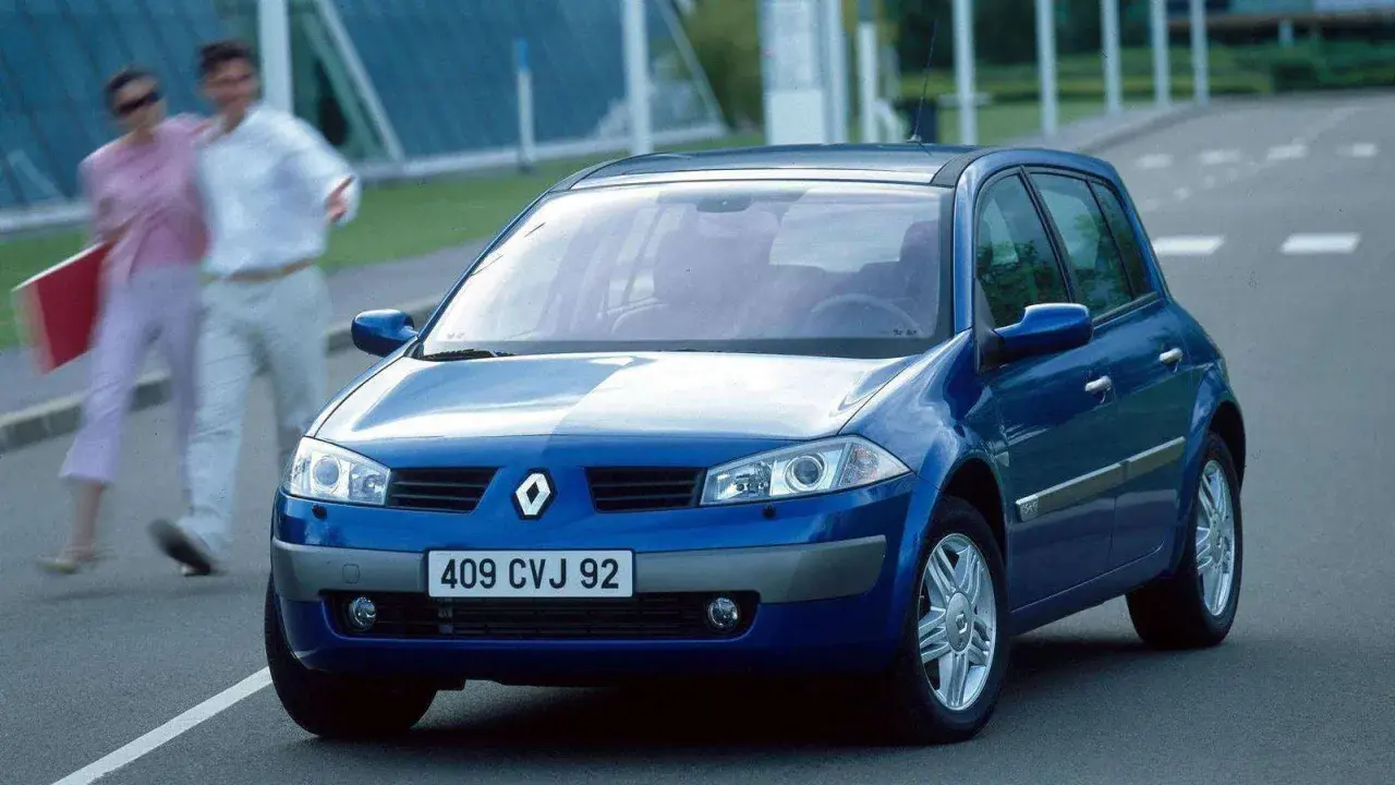Niebieski Renault Megane 2 na drodze, z parą ludzi w tle.