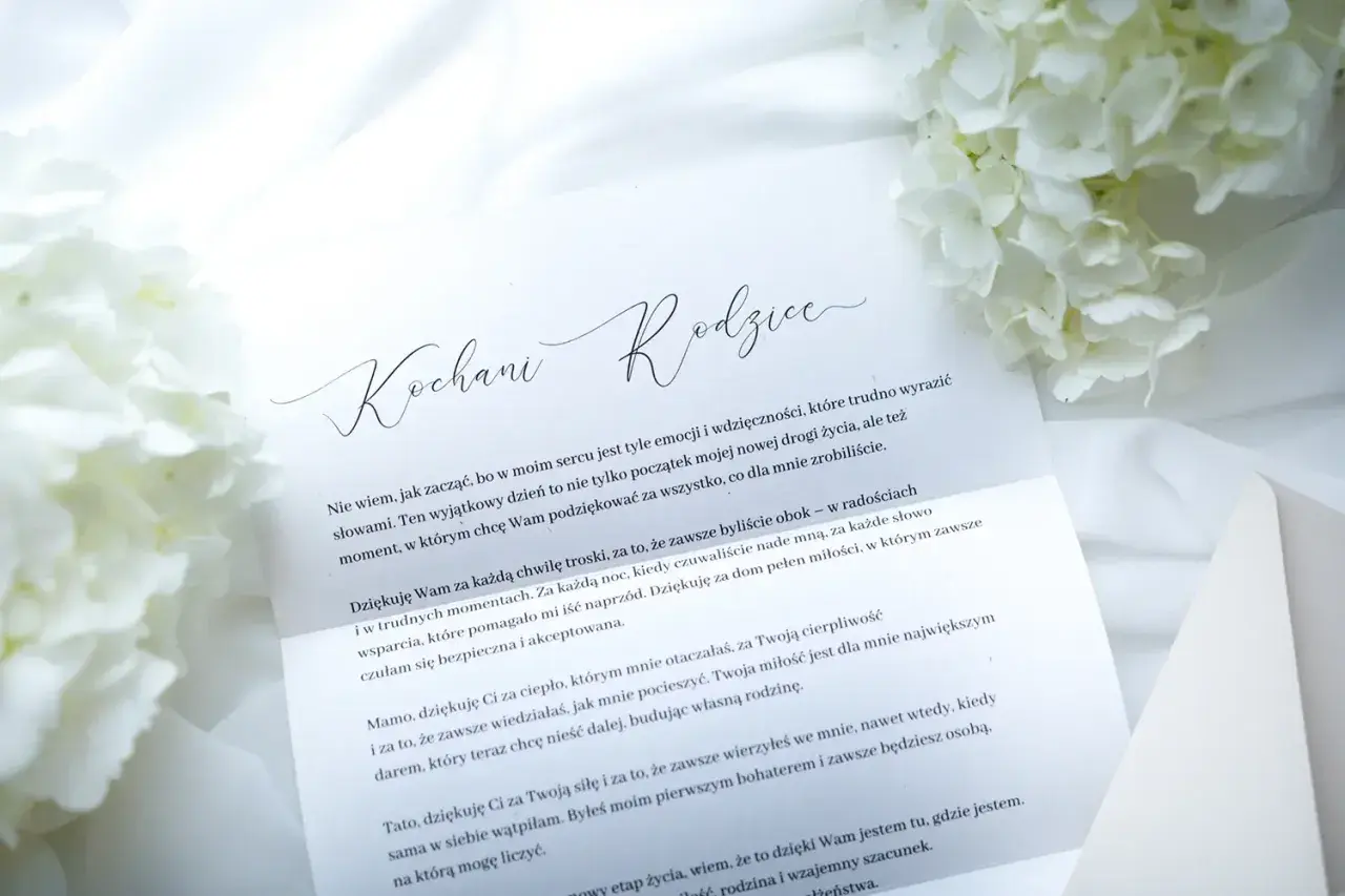 List do rodziców z podziękowaniami. Białe kwiaty i elegancka koperta tworzą tło dla wzruszających słów.