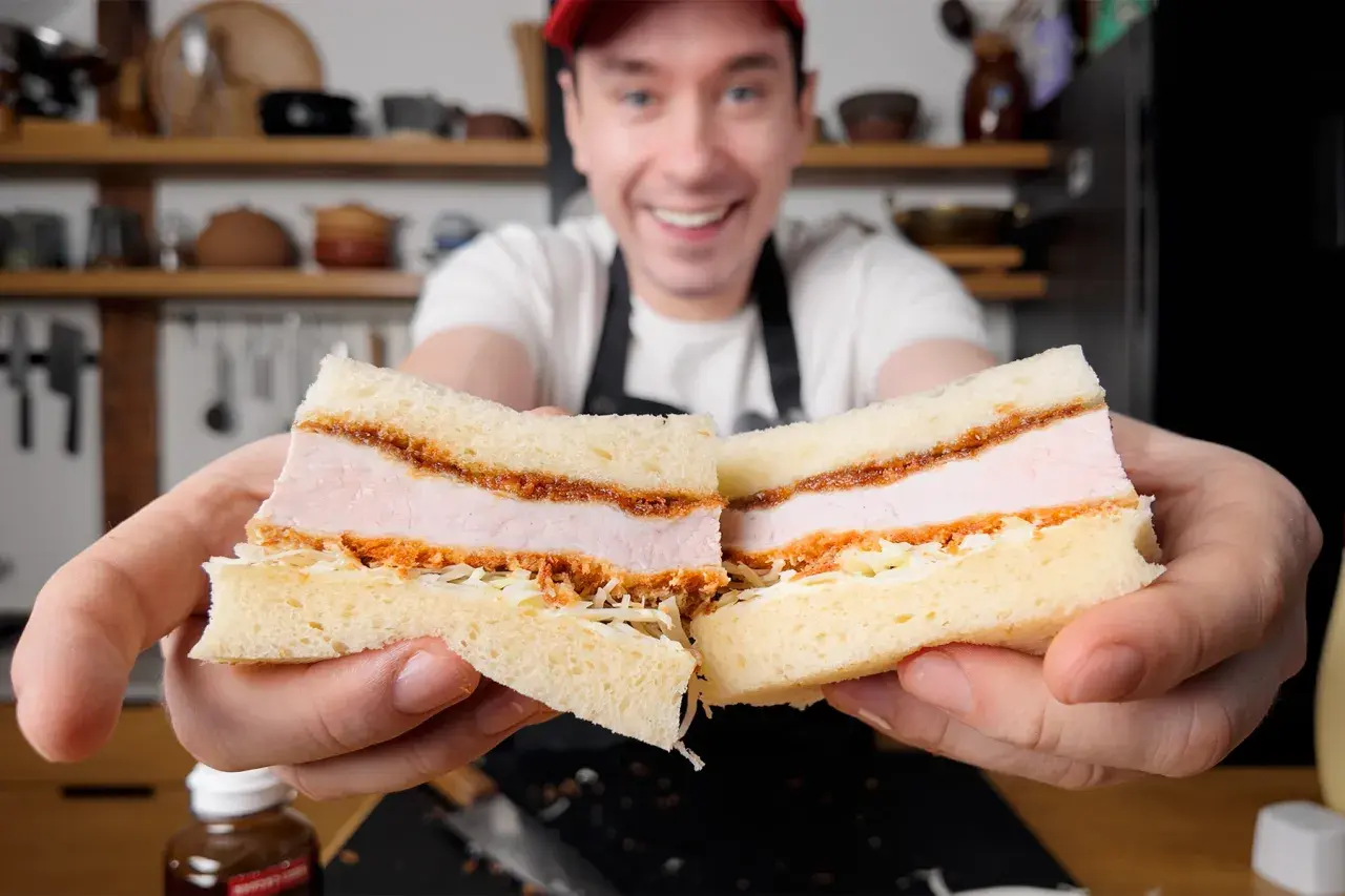 Uśmiechnięty mężczyzna prezentuje pyszne katsu sando z soczystym kotletem schabowym w panierce, delikatną kapustą i puszystym chlebem.