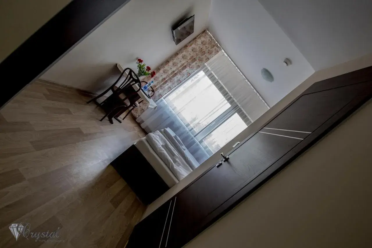Pokój w hotelu i restauracji Crystal: łóżko, stolik z krzesłami i kwiatami, okno z zasłonami.