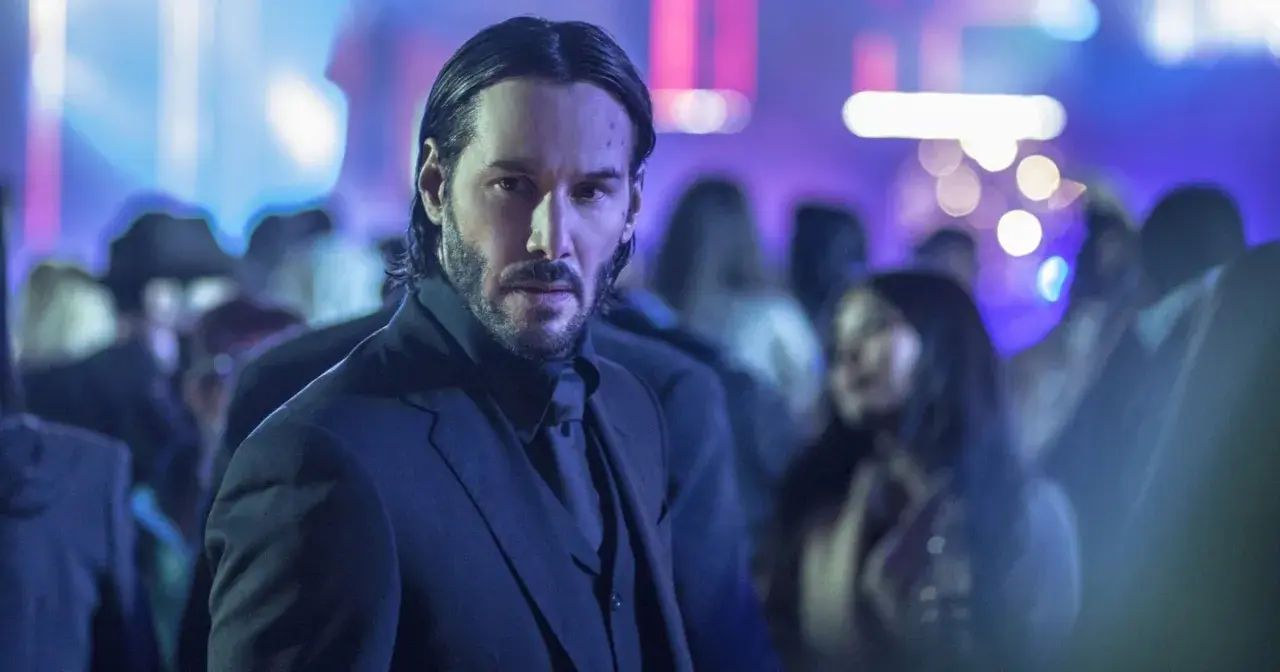 Keanu Reeves w garniturze, w tle rozmyte światła i tłum. Ikona kina akcji, znana z filmów takich jak John Wick.