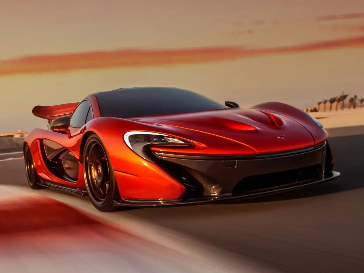 Czerwony McLaren P1 pędzi po pustynnej drodze o zachodzie słońca.