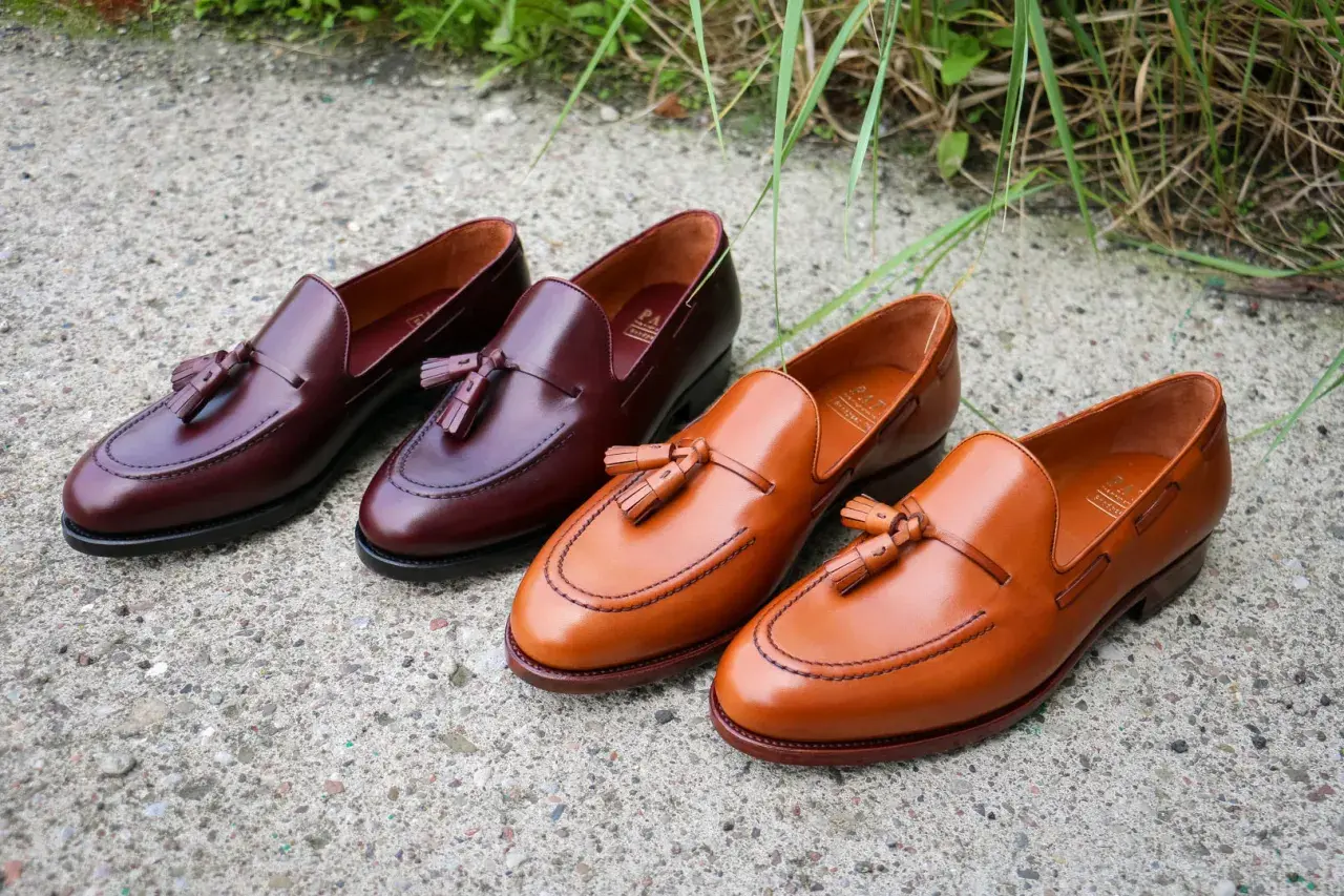 Eleganckie, skórzane loufersy z chwostami w kolorze koniaku i burgundu, ułożone na betonowej nawierzchni.