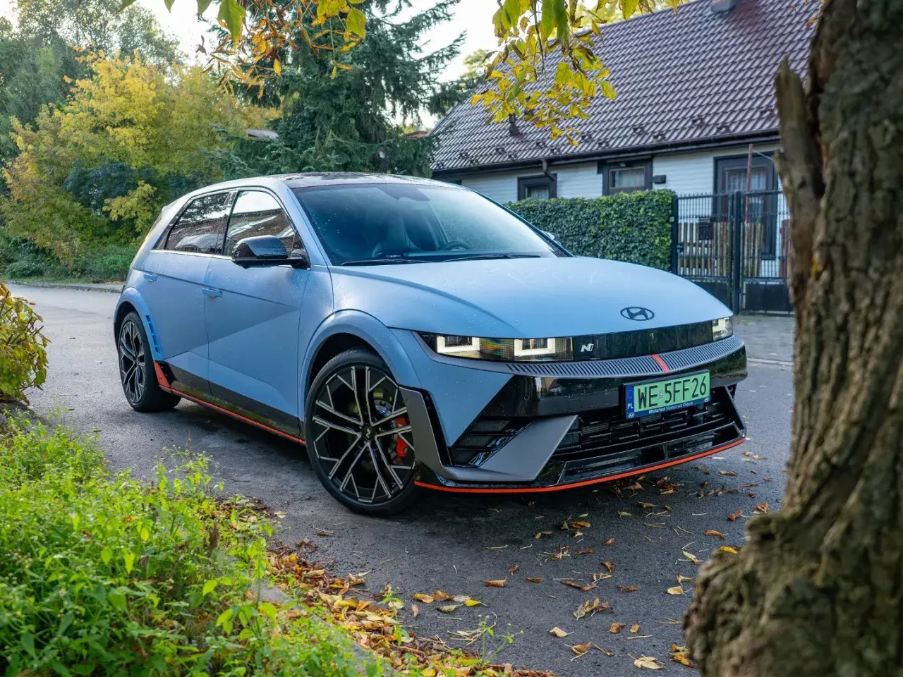 Niebieski Hyundai Ioniq 5 N z czerwonymi akcentami stoi na tle domu i drzew.