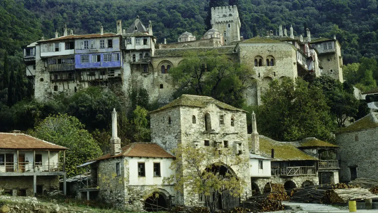 Kamienne budynki klasztorne na zboczu góry Athos, z niebieskim akcentem na jednym z nich.