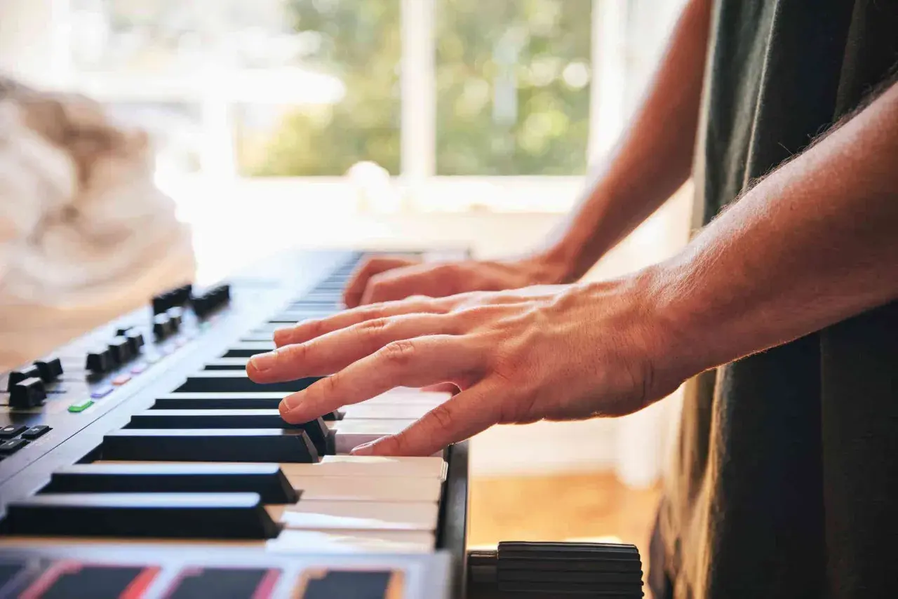 Dłonie grające na keyboardzie. To instrument muzyczny, który pozwala tworzyć melodie.