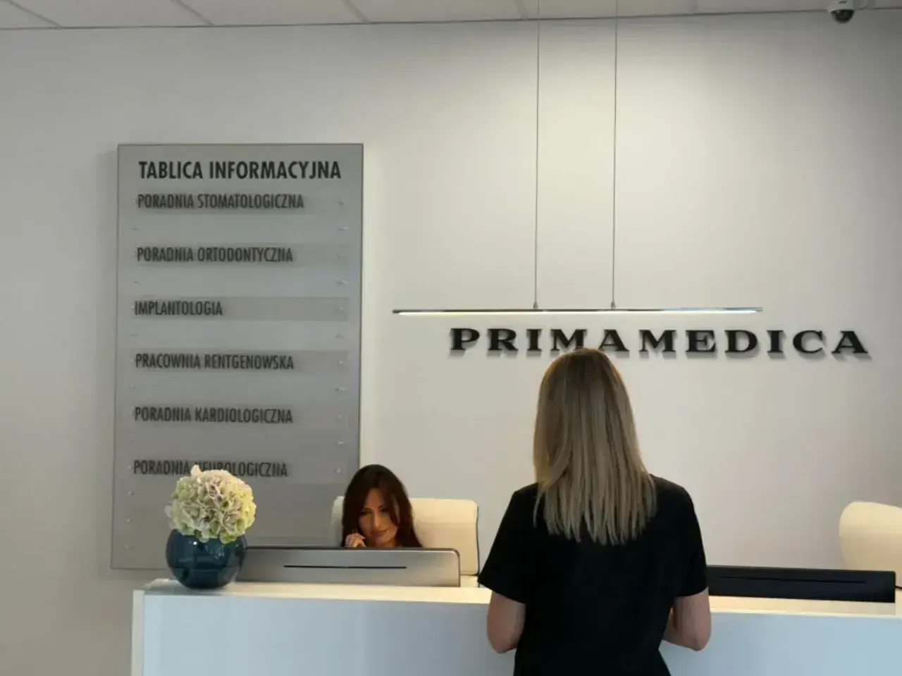 Recepcja gabinetu stomatologicznego Primamedica z tablicą informacyjną i pracownicą.