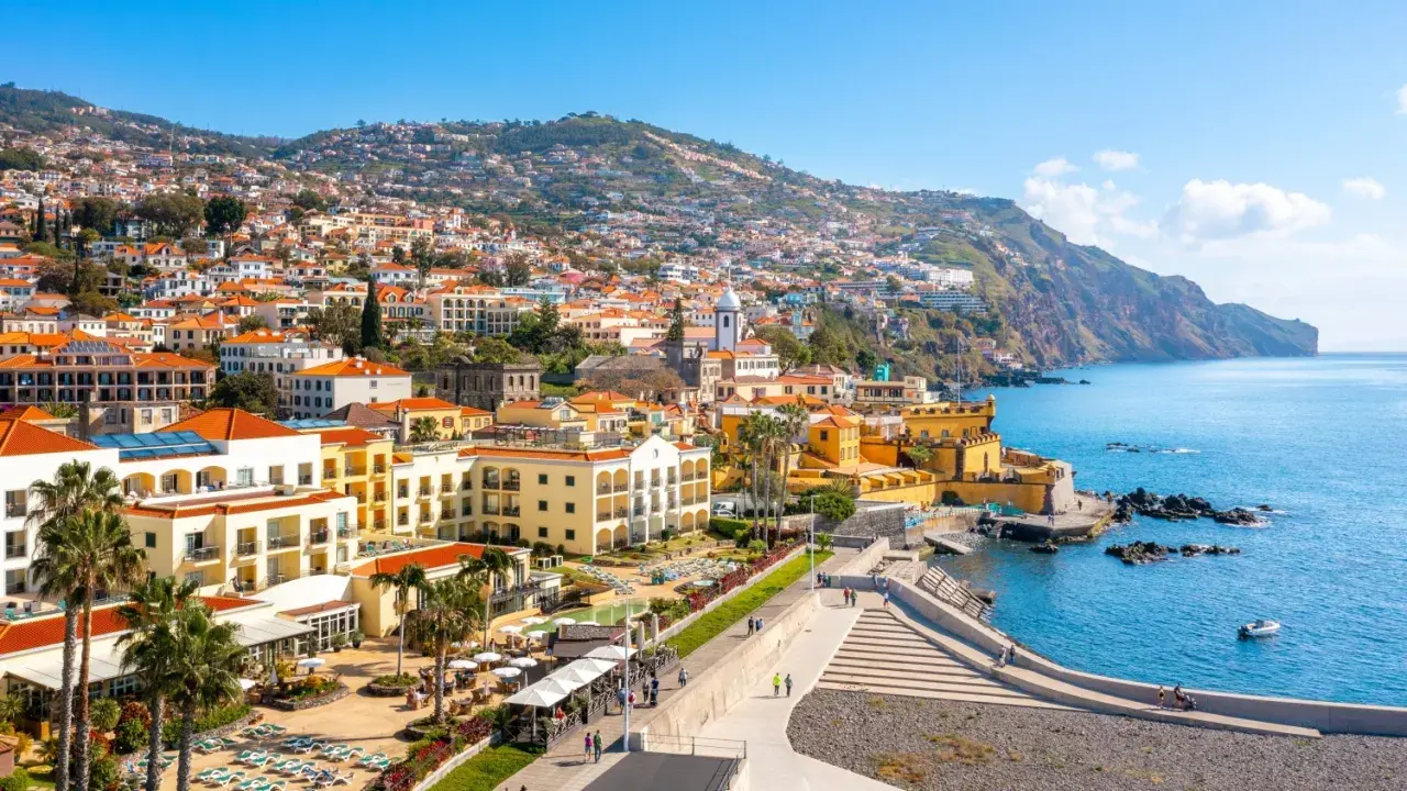 Widok na Funchal, stolicę Madery, z kolorowymi budynkami wznoszącymi się na zboczu góry, otoczonymi błękitnym oceanem.