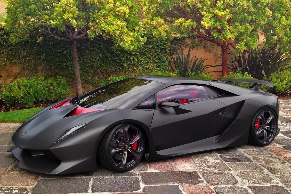 Matowy czarny Lamborghini Sesto Elemento z czerwonymi akcentami i wnętrzem, zaparkowany na brukowanej ścieżce wśród zieleni.