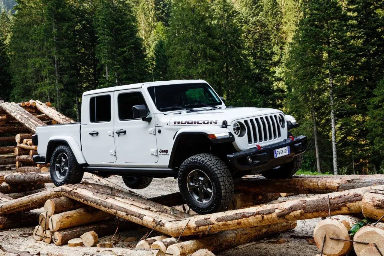 Biały jeep pickup Rubicon pokonuje przeszkodę z bali drewna w lesie.