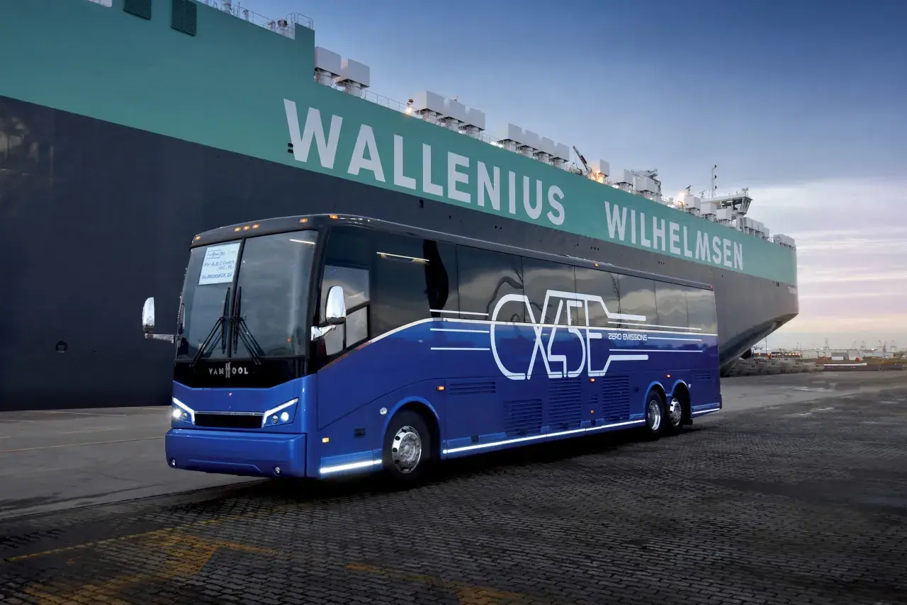 Niebieski autokar Van Hool CX45 z napisem "ZERO EMISSIONS" stoi przy ogromnym statku Wallenius Wilhelmsen.