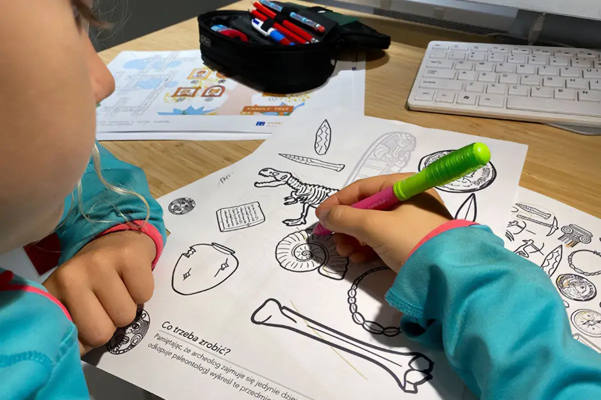 Dziecko koloruje edukacyjne karty pracy z dinozaurem i artefaktami.
