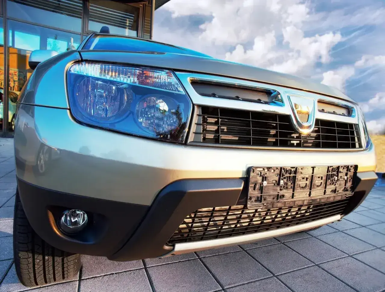 Złoty Dacia Duster 1.6 benzyna z chromowanym grillem i niebieskimi reflektorami, gotowy na przygodę pod błękitnym niebem.