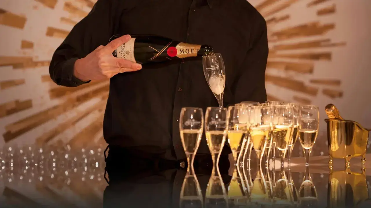Kelner nalewa szampan Moët & Chandon do kieliszków, przygotowując się do wesela.