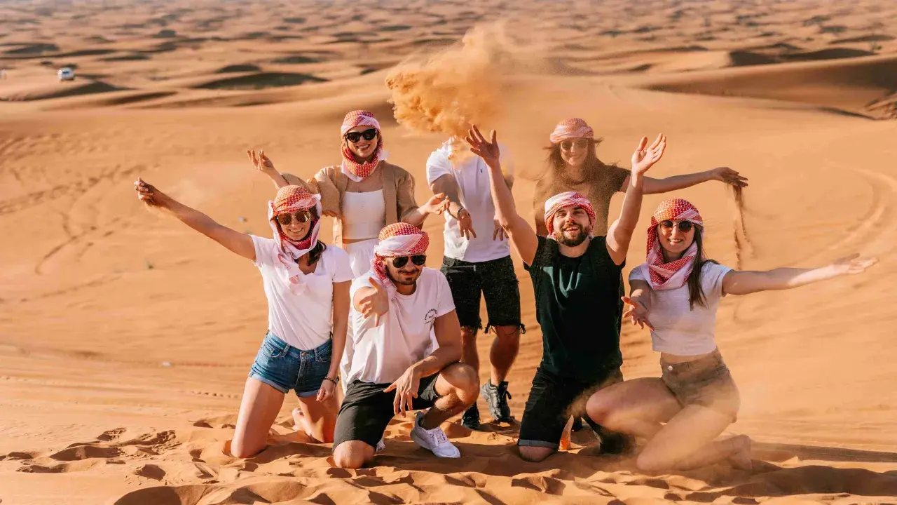 Grupa przyjaciół w tradycyjnych arabskich chustach bawi się piaskiem na pustyni. Wspaniałe wspomnienia z Dubaju w styczniu.