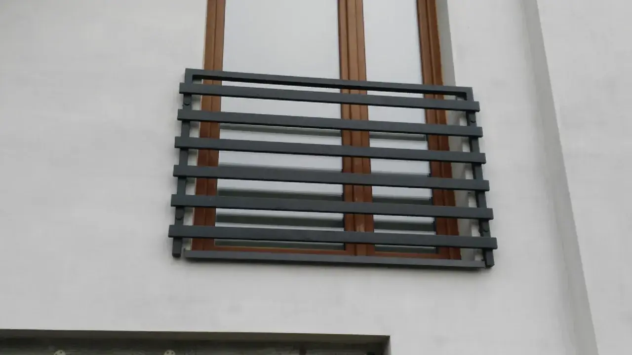 Nowoczesne balkony francuskie z ciemnoszarymi, poziomymi barierkami na tle białej ściany i brązowych okien.