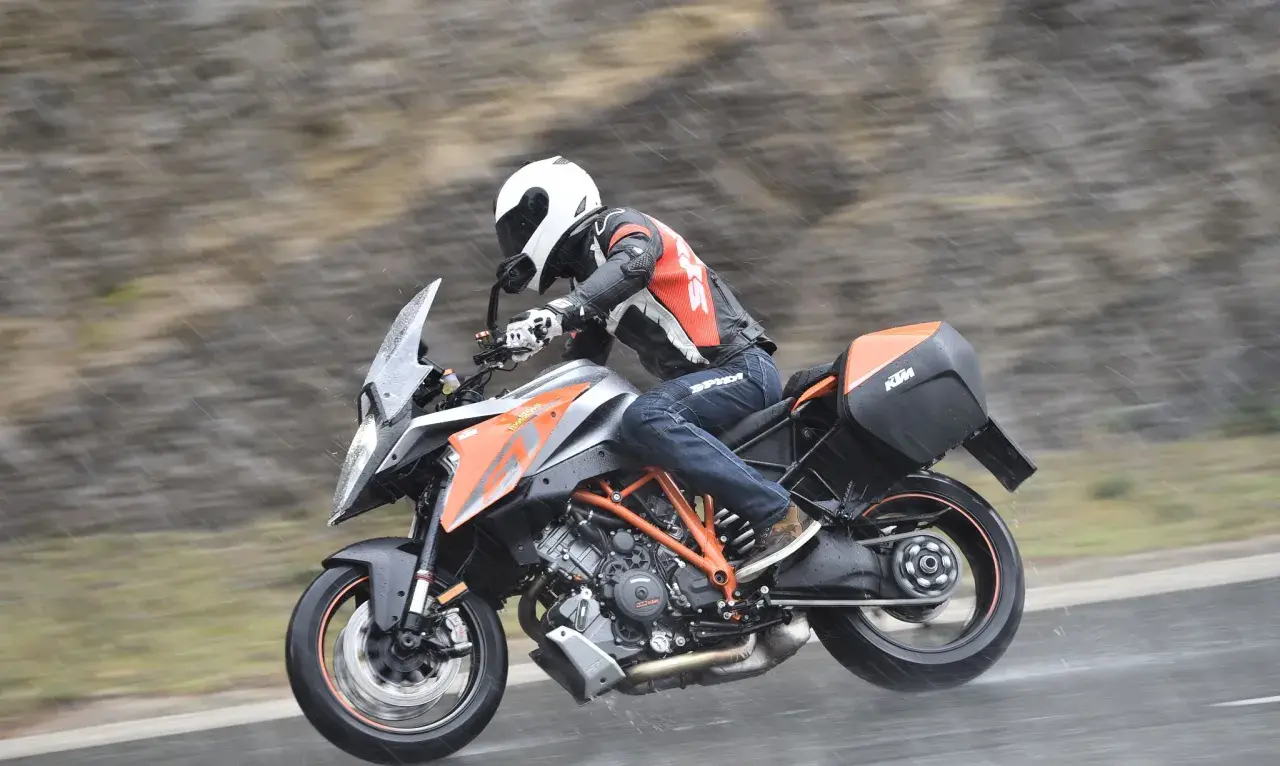 Motocyklista w kasku i kombinezonie śmiga na KTM Super Duke 1290 GT w deszczu.