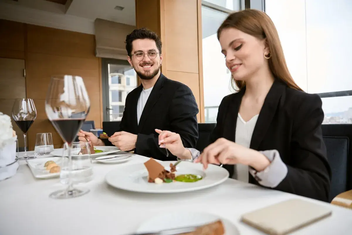 Elegancki strój na kolację do restauracji. Para w czarnych marynarkach delektuje się wykwintnym deserem przy kieliszkach czerwonego wina.