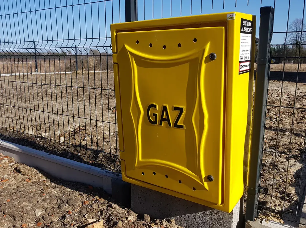 Żółta skrzynka gazowa z napisem "GAZ" przy ogrodzeniu. Zastanawiasz się, ile kosztuje przyłącze gazu?