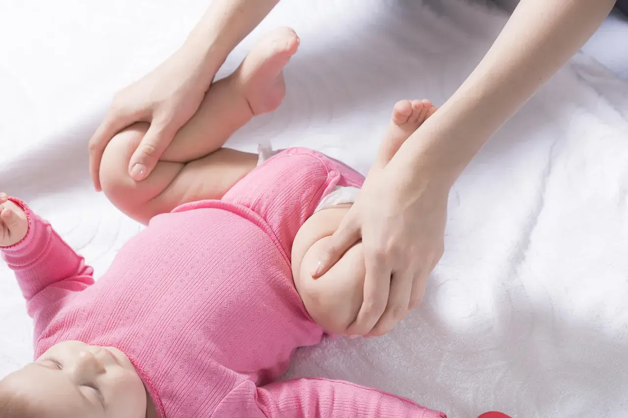 Delikatne ruchy dłoni badają bioderka niemowlęcia, sprawdzając pod kątem dysplazji.