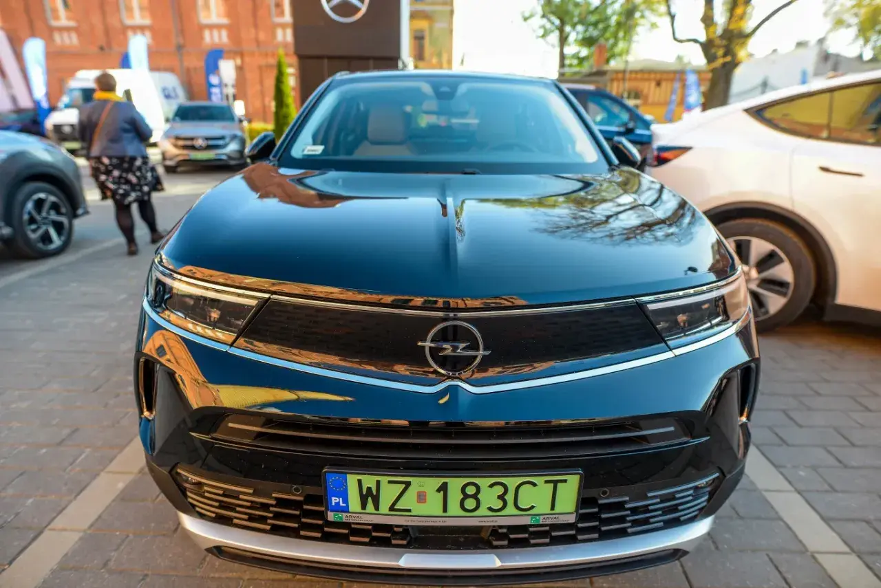 Czarny Opel z zieloną tablicą rejestracyjną WZ 183CT na tle innych samochodów.