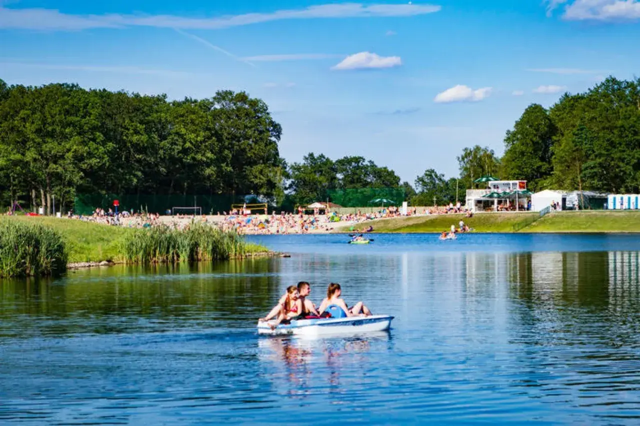Rodzina na rowerku wodnym na jeziorze, plaża pełna ludzi, las i budynki w tle. Idealne miejsce gdzie nad wodę Dolny Śląsk.
