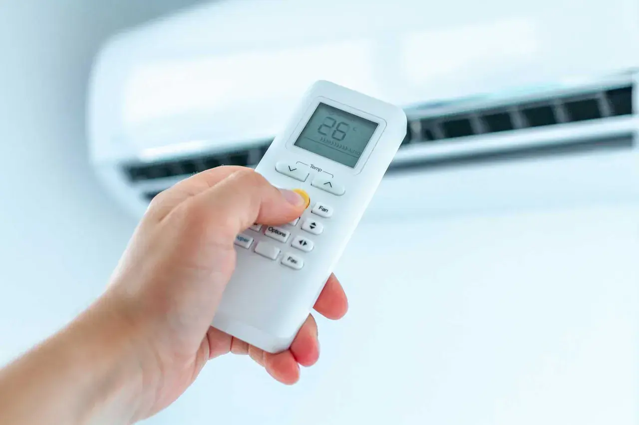 Dłoń trzymająca pilot do klimatyzatora, ustawiająca temperaturę. Ogrzewanie klimatyzatorem to komfort.