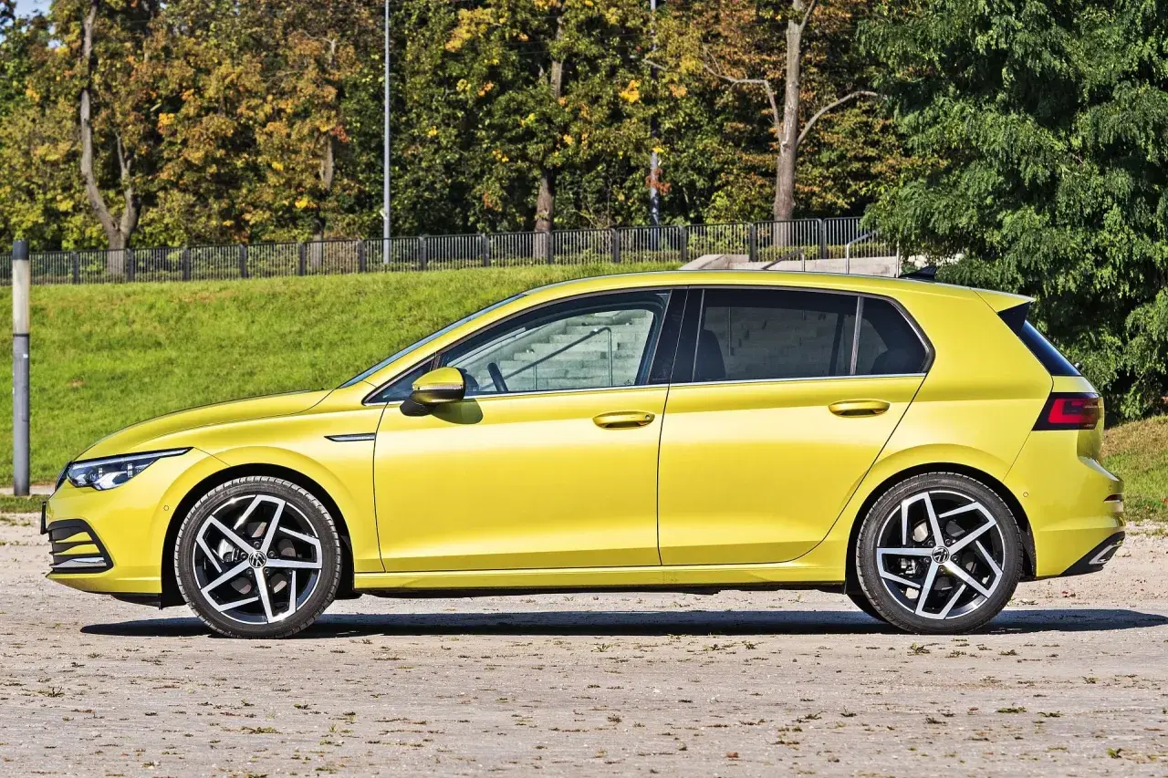 Żółty hatchback Volkswagen Golf VIII z przyciemnianymi szybami stoi na tle zieleni i drzew.