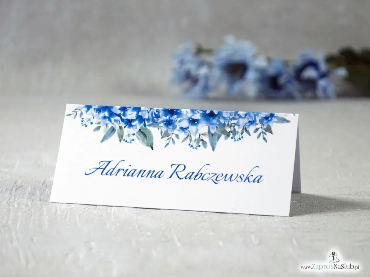 Eleganckie winietki dla usługodawców z motywem niebieskich kwiatów. Na białej kartce widnieje imię i nazwisko "Adrianna Rabczewska".