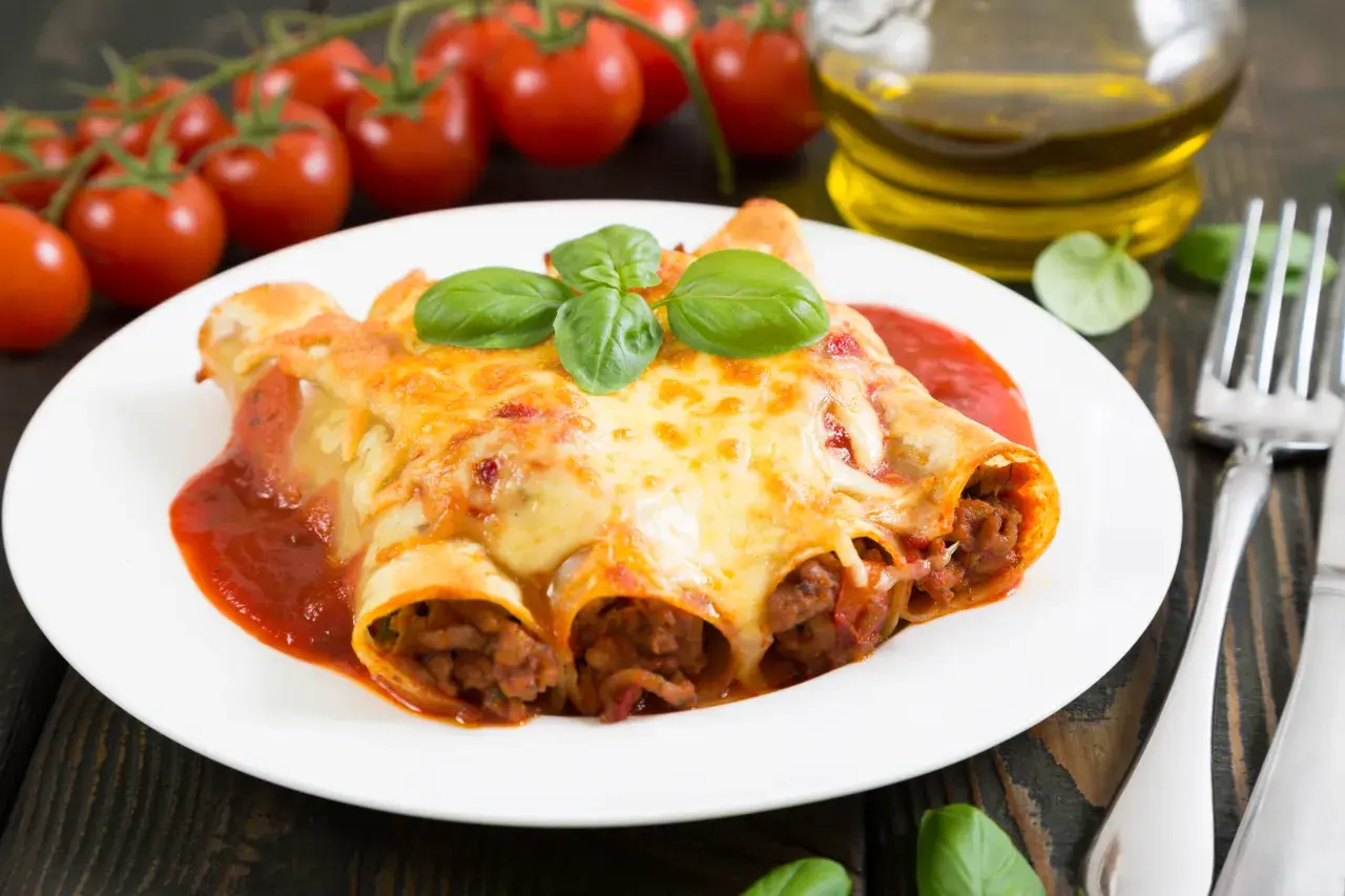 Cannelloni kontra naleśniki z mięsem: zapieczone w sosie pomidorowym i serze, ozdobione bazylią. Obok pomidorki i oliwa.
