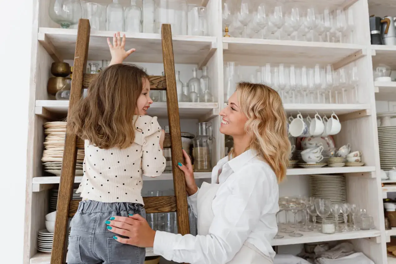 Mama i córka przy regale pełnym naczyń. W górnych szafkach kuchennych trzymamy rzadziej używane, ozdobne kieliszki i filiżanki.