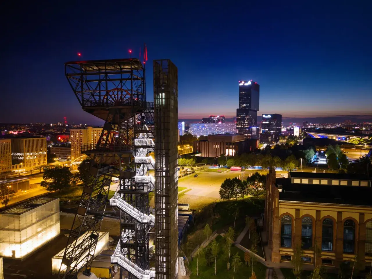 Wieżowiec kopalni węgla obok nowoczesnych budynków tworzy kontrast w nocnym megapolis.