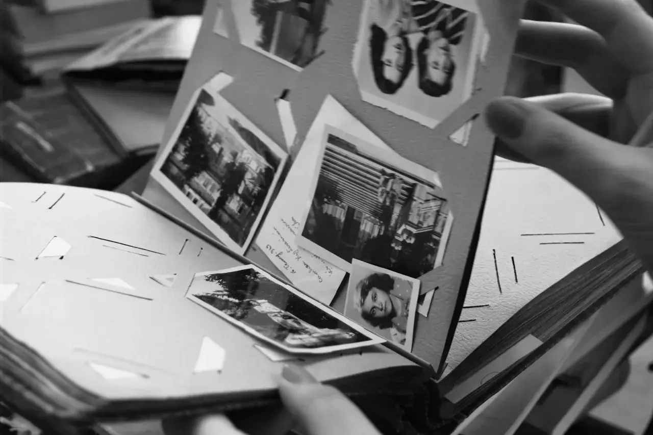 Odkryj, jak zrobić fotoksiążkę, przeglądając stare zdjęcia w albumie. Ręka trzyma kartę z portretami i krajobrazami.