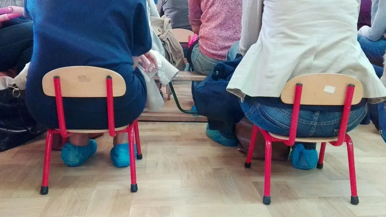 Dostateczny, jaka to ocena? Dzieci siedzą na małych krzesełkach w niebieskich ochraniaczach na buty.