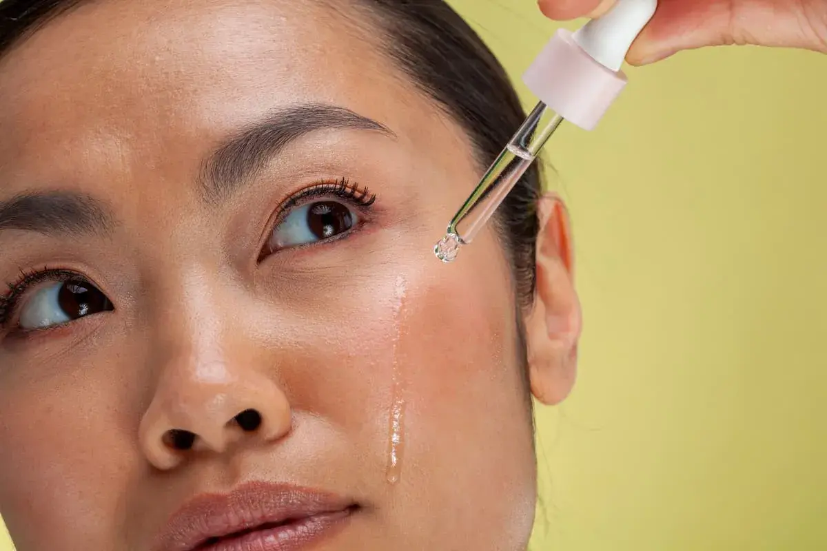 Kropla serum z pipetki spada na policzek kobiety. To może być retinol, który co to jest i jak działa, warto sprawdzić.
