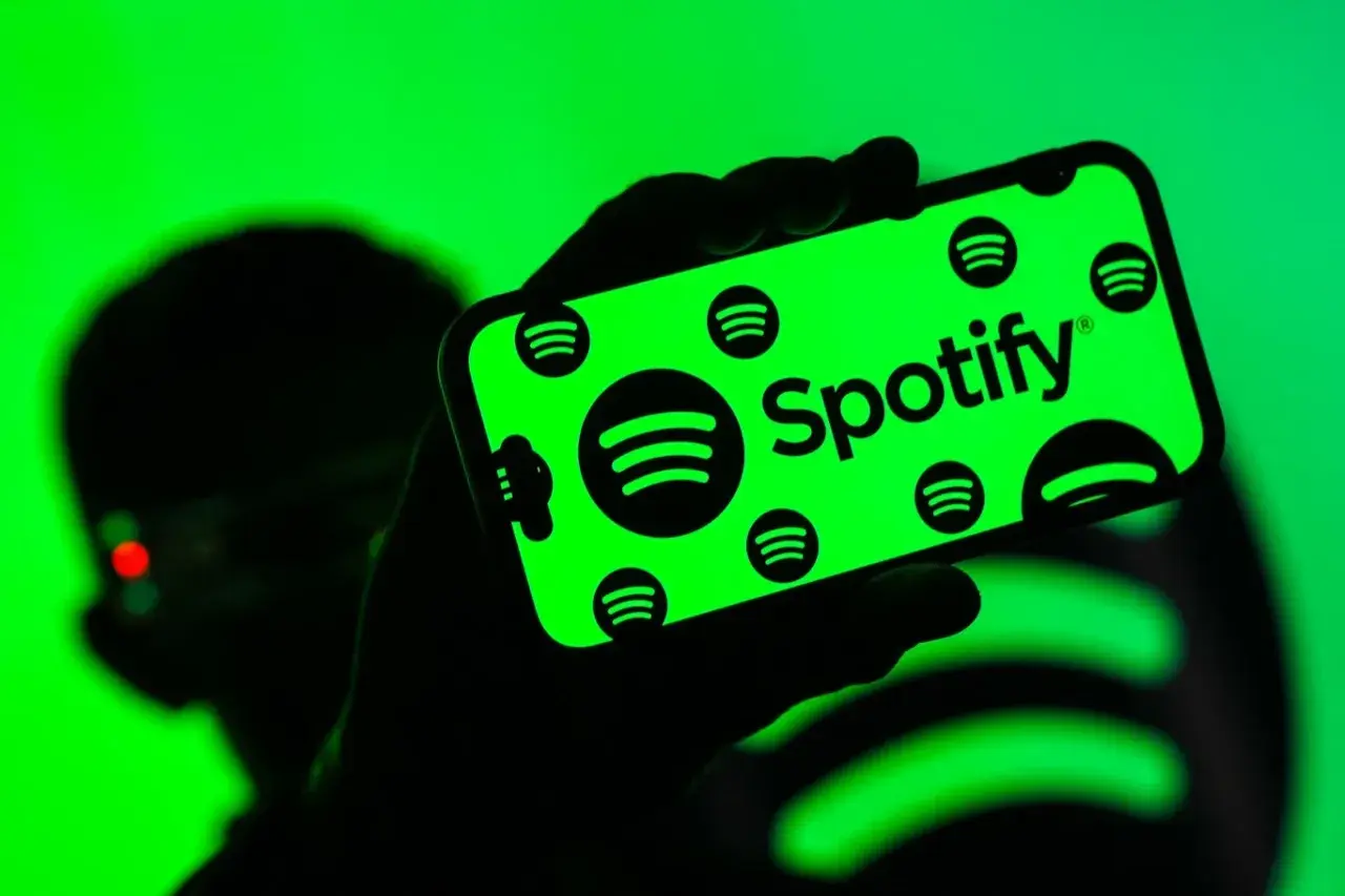 Dłoń trzyma smartfon z zielonym ekranem, na którym widnieje logo Spotify. Użytkownik cieszy się doskonałą spotify jakość dźwięku.