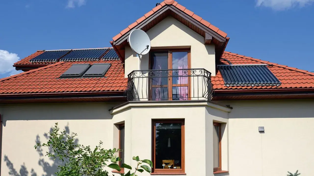 Elegancki wykusz w domu z balkonem i anteną satelitarną. Na dachu widoczne kolektory słoneczne.