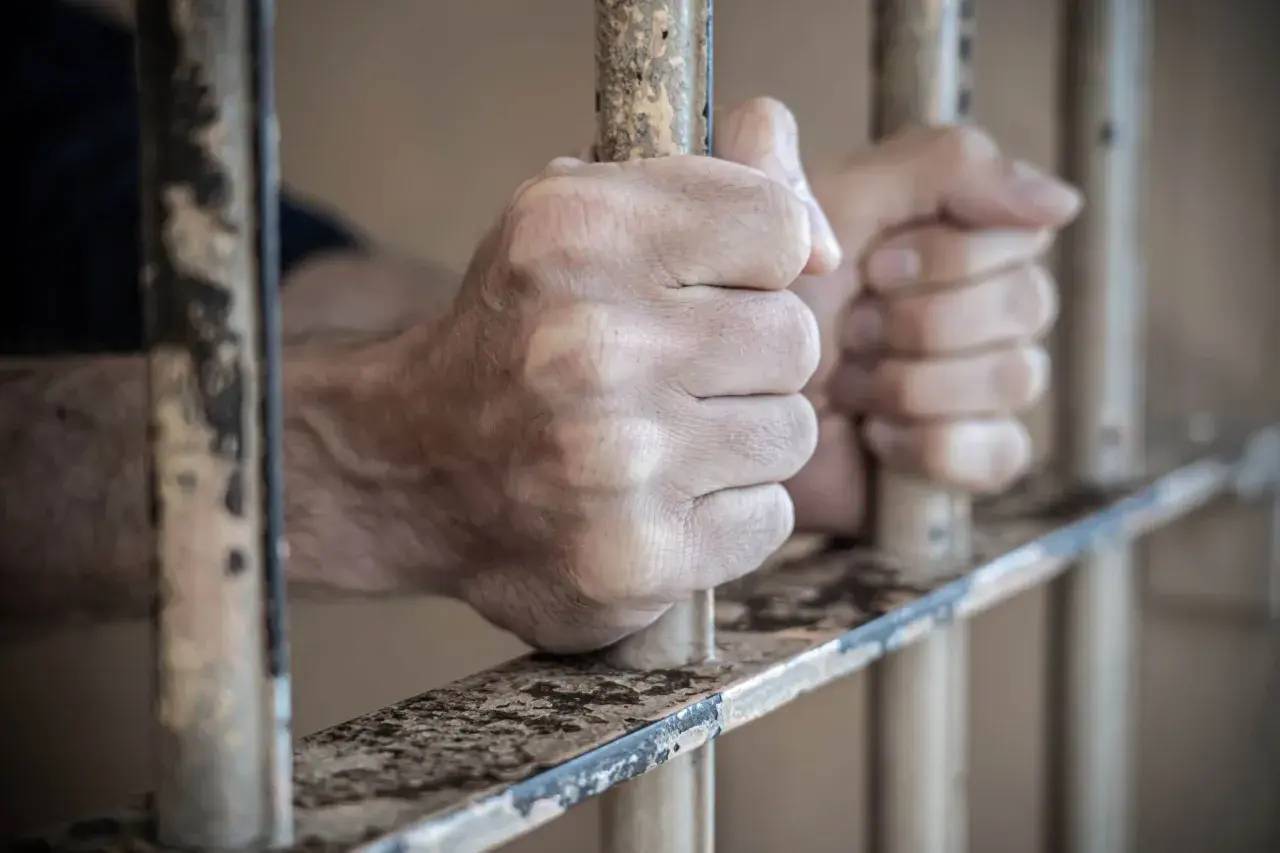 Dłonie zaciskają się na kratach aresztu śledczego. Widok zza prętów.
