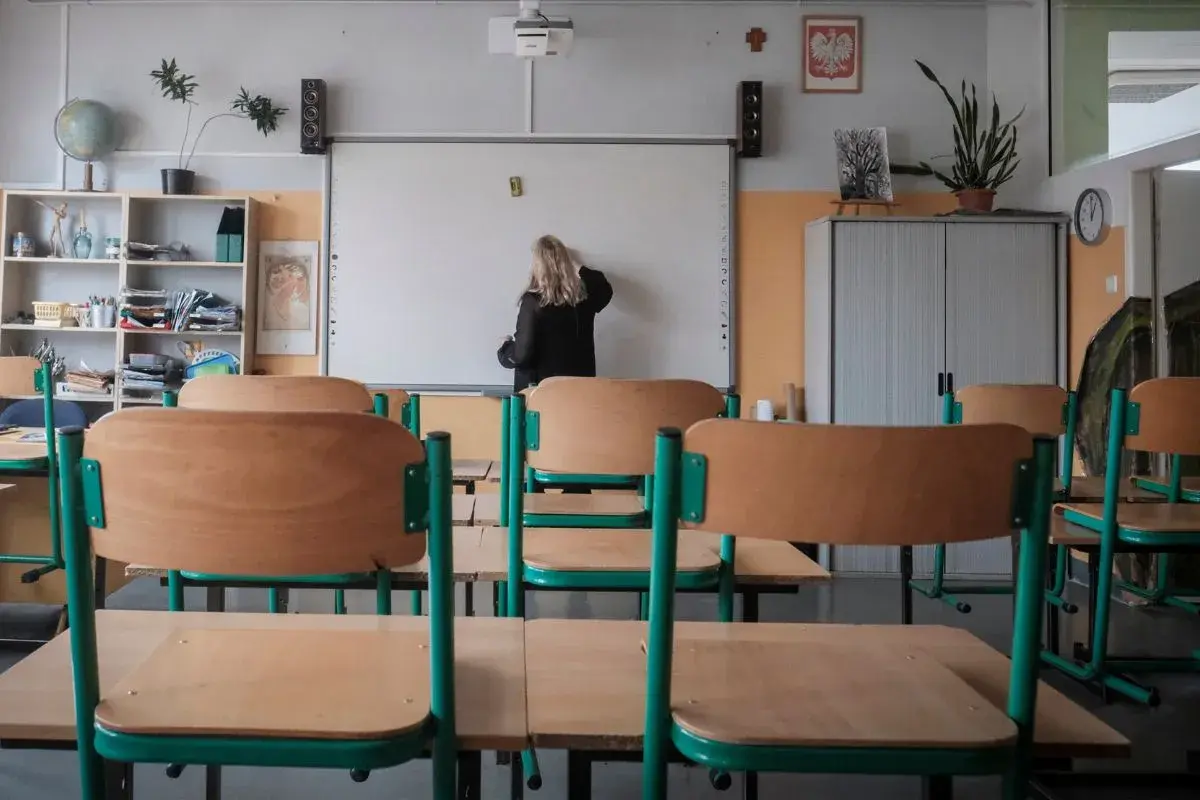 Nauczycielka przy tablicy, zastanawia się, ile zarabia przedszkolanka. Puste ławki w sali lekcyjnej.
