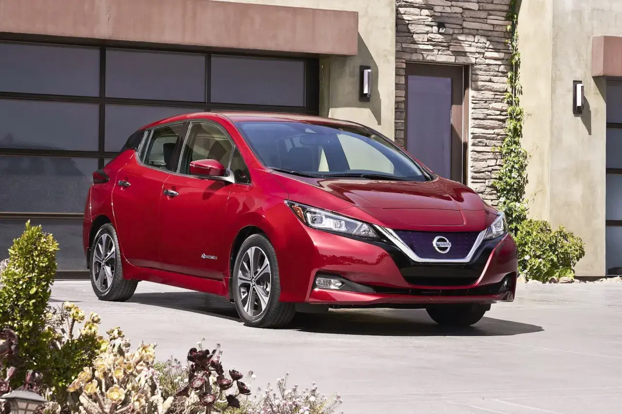 Czerwony Nissan Leaf przed nowoczesnym domem. Sprawdź atrakcyjną nissan leaf cena i wybierz swój wymarzony samochód elektryczny.