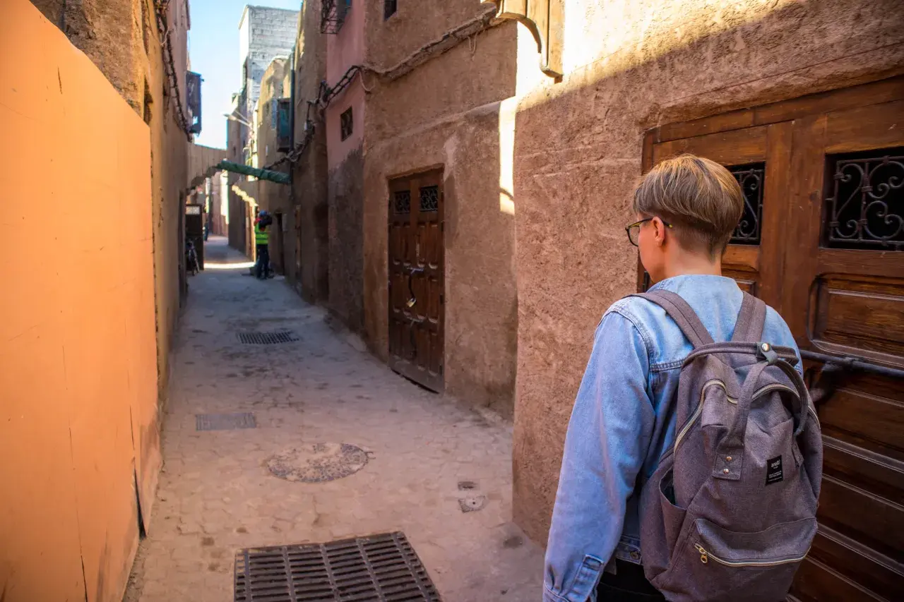 Młoda osoba z plecakiem idzie wąską uliczką w Marrakeszu. Czy w Marrakeszu jest bezpiecznie? Tak, zwiedzanie jest przyjemne.